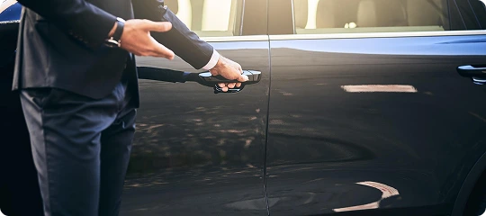 Professional chauffeur in a suit opening the door of a black luxury vehicle, showcasing Prestige Ride's personal chauffeur service in Chicago