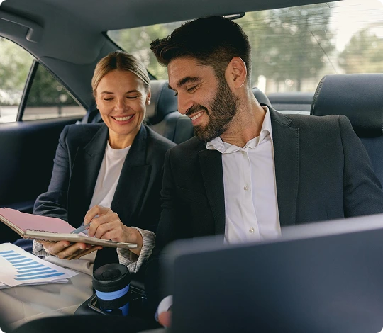 Smiling businesswoman and businessman reviewing documents and working together inside the backseat of a luxury vehicle
